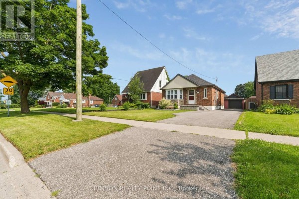 View of the house from the sidewalk, showing a green lawn and surrounding houses. - 503 Athol Street E, Oshawa