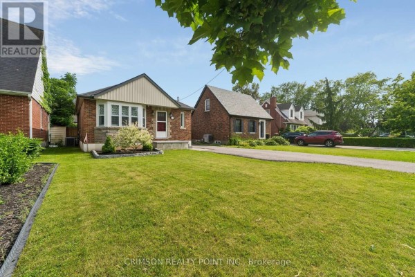 Side view of the house, showing a green lawn and trees in the foreground. - 503 Athol Street E, Oshawa