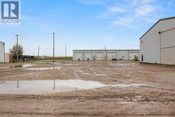 View of industrial buildings from a muddy lot with puddles under a partly cloudy sky. - 5030 50 Avenue, Lougheed