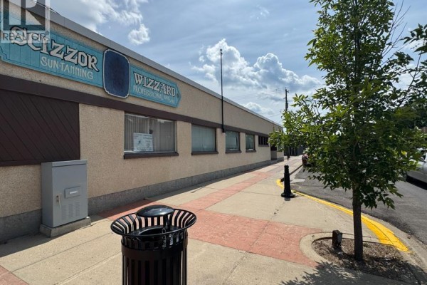 Side view of the commercial building exterior with trees and sidewalk in the foreground. - 5033 50ave, Ponoka
