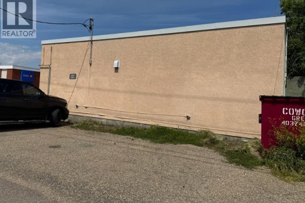 Rear exterior of the commercial building with a gravel lot, grass, and a red dumpster. - 5033 50ave, Ponoka
