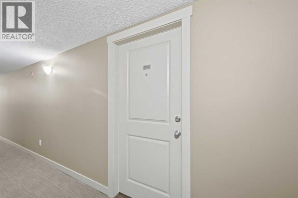 Hallway inside the building leading to unit 504, with beige walls and a white door. - 504, 10 Kincora Glen Park Nw, Calgary