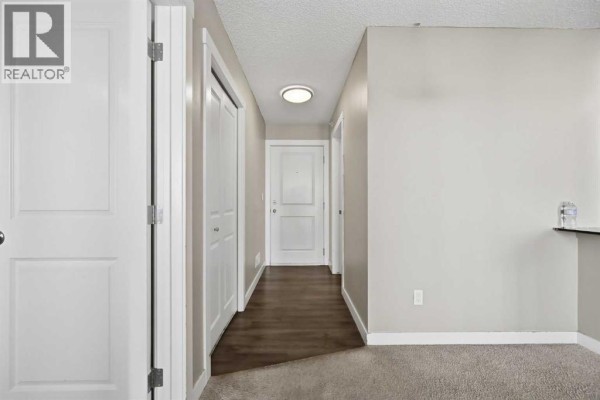 Interior hallway with light gray walls, dark wood floors, white doors, and beige carpet. - 504, 10 Kincora Glen Park Nw, Calgary