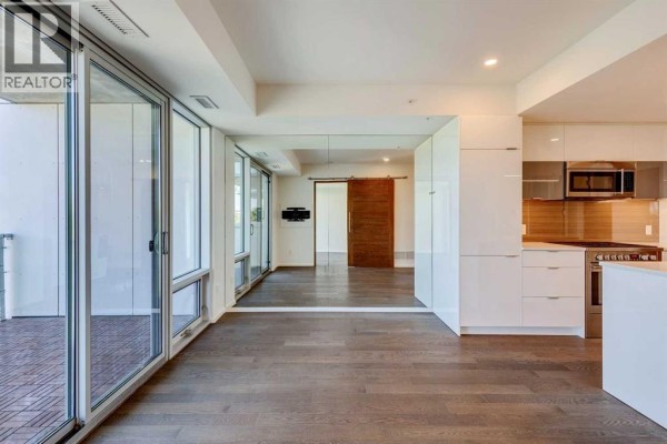 Open concept living area with floor-to-ceiling windows, mirrored wall, and a wooden sliding door. - 504, 1020 9 Avenue Se, Calgary