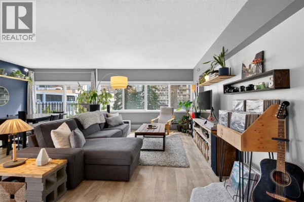 Living room and dining area with a sectional sofa, coffee table, and dining table. - 504, 1209 6 Street Sw, Calgary