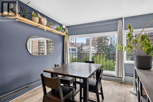 Dining area with a dark wood table, black chairs, and a large window view. - 504, 1209 6 Street Sw, Calgary