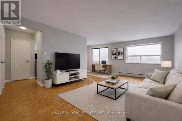 Living room with beige sofa, coffee table, television, and large windows with wooden floors. - 504 - 1780 Lawrence Avenue E, Toronto