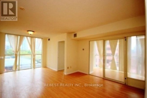 Living room with light wood floors, cream walls, floor-to-ceiling windows with sheer curtains, and mirrored closet doors. - 504 - 265 Enfield Place, Mississauga