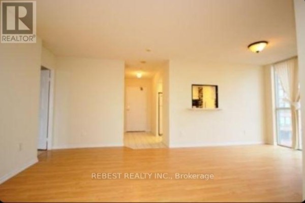 View of an open-concept living space with light wood floors, cream walls, and a pass-through to another room. - 504 - 265 Enfield Place, Mississauga