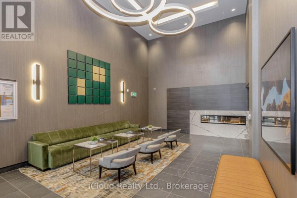 Building lobby with a long green sofa, chairs, modern fireplace, and artwork. - 504 - 95 Dundas Street, Oakville