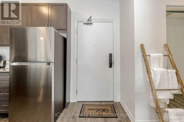 Apartment entrance with stainless steel refrigerator, dark wood cabinets, and white door. - 504 - 95 Dundas Street, Oakville