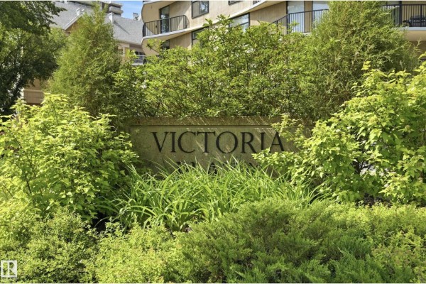 Stone monument sign with carved letters spelling "VICTORIA PLACE" surrounded by lush green foliage. - #504 11710 100 Av Nw, Edmonton