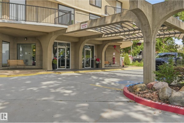 Covered entrance to apartment building with concrete arches, glass doors, and benches. - #504 11710 100 Av Nw, Edmonton
