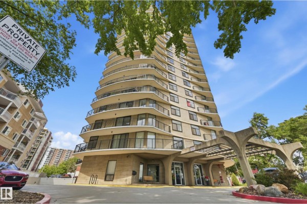 Low-angle view of a beige apartment building's curved facade with balconies and a concrete entrance. - #504 11710 100 Av Nw, Edmonton