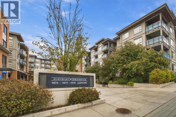 Exterior view of the District Crossing apartment complex entrance sign on a paved driveway. - 504 1677 Lloyd Avenue, North Vancouver