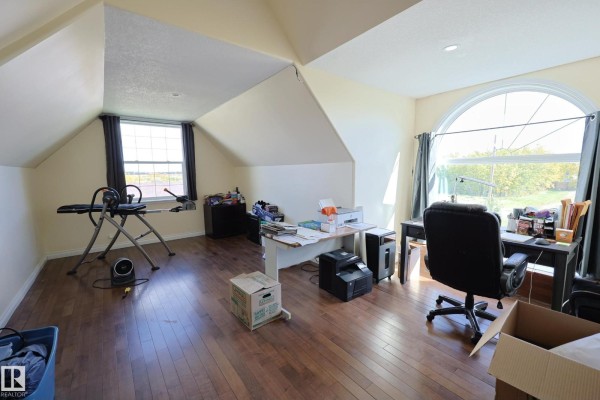 Attic room with sloped ceilings, hardwood floors, a large arched window, and office furniture. - 504 4 St, Alcomdale