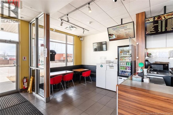 Counter area of a commercial space with menu boards, refrigerator, and seating booths. - 504 Champlain Street Unit# A, Dieppe