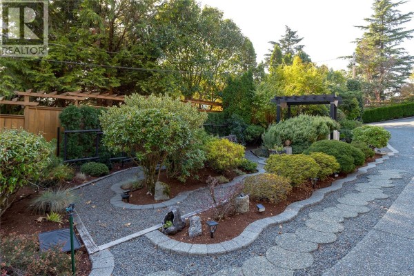 Curving gravel pathway through a meticulously landscaped garden with various shrubs and small trees. - 504 Langvista Dr, Langford