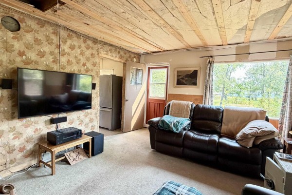 Living room with a TV, sound system, refrigerator, and a leather sofa facing the window. - 5040 49 St, Drayton Valley