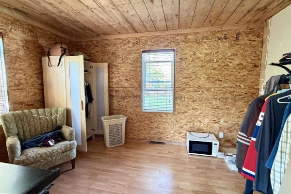 Bedroom with OSB walls, a window, armchair, wardrobe, and microwave on the floor. - 5040 49 St, Drayton Valley