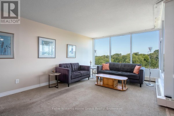 Living room with two dark grey sofas, a coffee table, and a wall of windows with a green view. - 505 - 23 Woodlawn Road E, Guelph