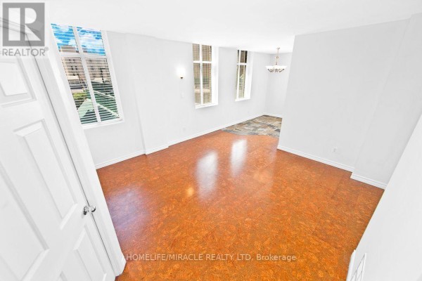 Living room with cork flooring, white walls, and two windows overlooking buildings. - 505 - 36 James Street S, Hamilton
