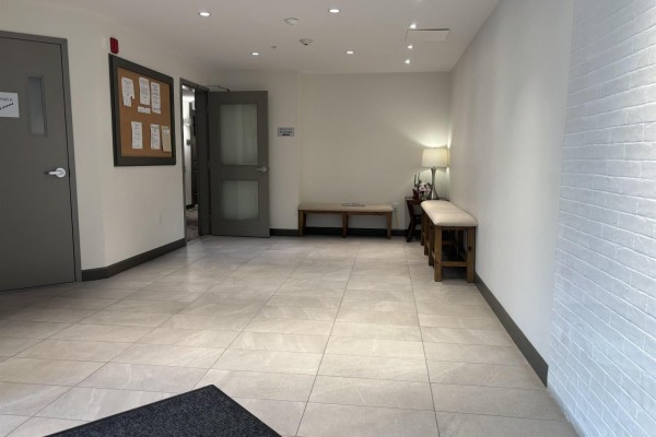 Apartment building lobby with beige tiled floor, cork bulletin board, and two wooden benches. - 505 3535 146a Street, Surrey