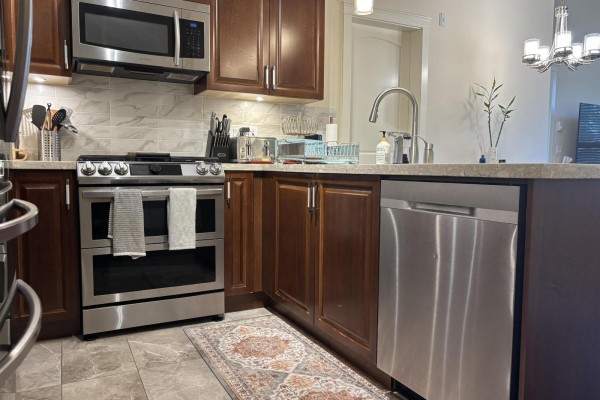 Kitchen view with stainless steel stove, dishwasher, and wooden cabinets. Patterned rug on floor. - 505 3535 146a Street, Surrey