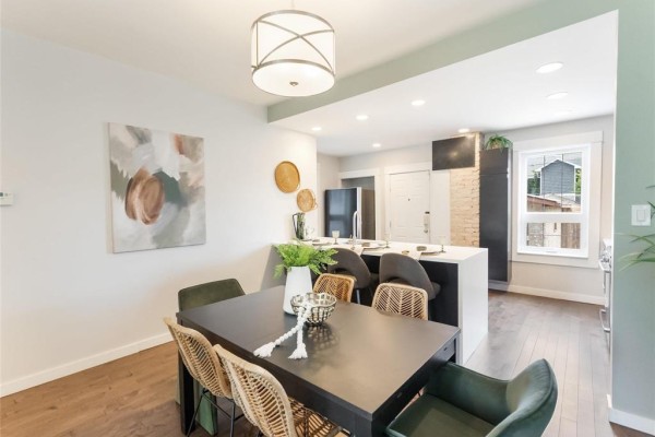 Kitchen with a dark dining table, island with bar stools, and stainless steel refrigerator. - 505 Basswood Place, Winnipeg
