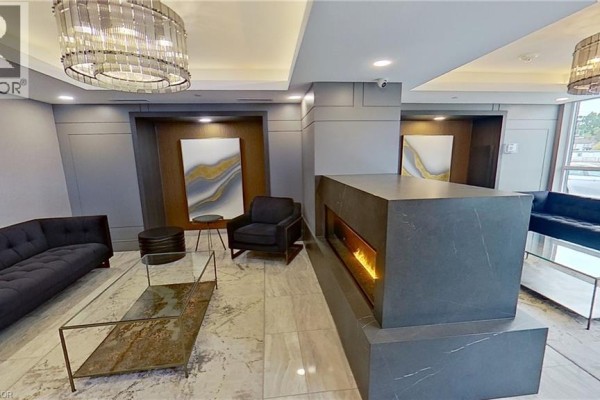 Apartment building lobby with grey walls, marble tile floors, modern furniture, and a decorative fireplace. - 5055 Greenlane Street Unit# 337, Beamsville