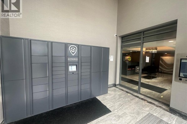 Grey package locker system installed in the apartment building's entryway next to a glass door. - 5055 Greenlane Street Unit# 337, Beamsville