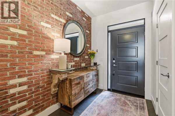 Entryway with a dark teal door, a wooden console table, and brick wall. - 5056 New Street Unit# 4, Burlington