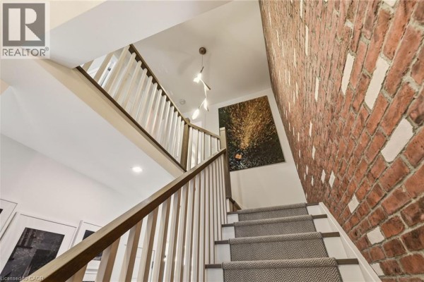 Entryway with brick wall, round mirror, console table, and tulips in a vase. - 5056 New Street Unit# 4, Burlington