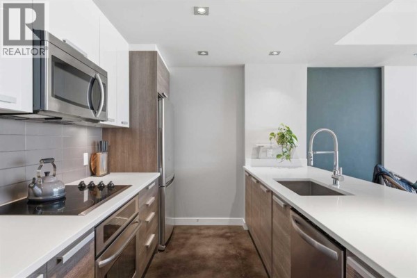 Open concept kitchen and living area with city views through large windows. - 506, 235 9a Street Nw, Calgary