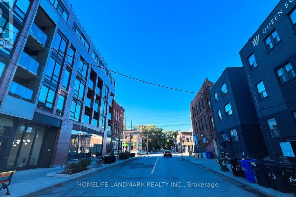 Street view looking down a city street with apartment buildings on both sides and blue sky above. - 506 - 246 Logan Avenue, Toronto
