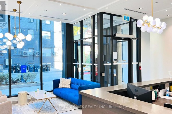 Building lobby with a blue velvet sofa, modern chairs, marble-look table, and large windows. - 506 - 246 Logan Avenue, Toronto