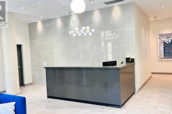 Building reception desk with a dark grey counter, marble-look wall, and modern chandelier. - 506 - 246 Logan Avenue, Toronto
