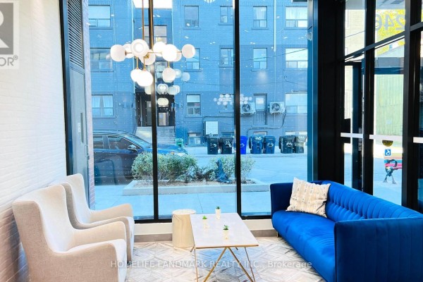 Lobby seating area with a blue sofa, beige chairs, and view of the street through large windows. - 506 - 246 Logan Avenue, Toronto