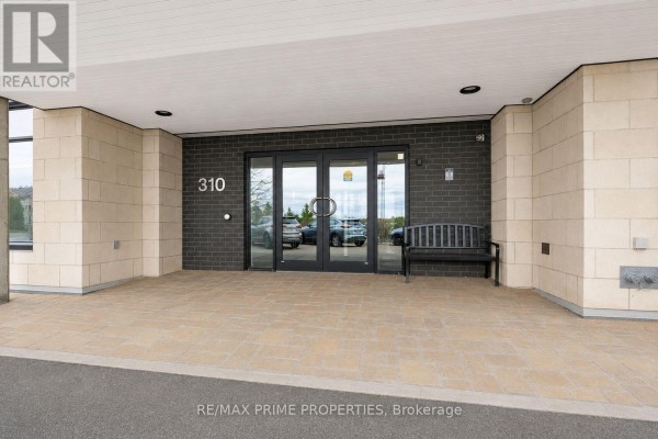 Entrance to building 310 with double glass doors, tan stone pillars, and a dark brick facade. - 506 - 310 Centrum Boulevard, Ottawa