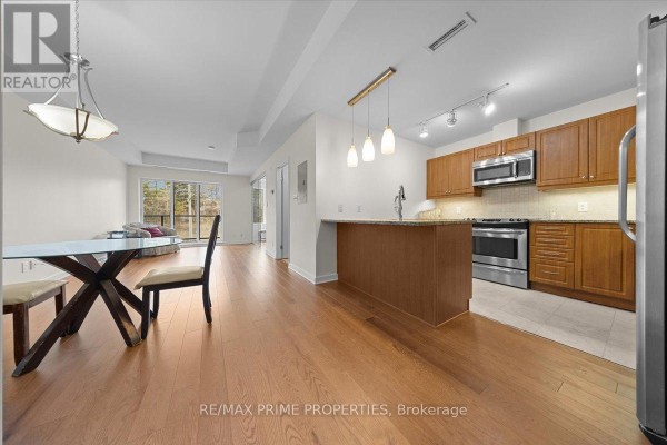 Interior view of an apartment hallway showing a wooden front door, hardwood floors, and an open living area. - 506 - 310 Centrum Boulevard, Ottawa