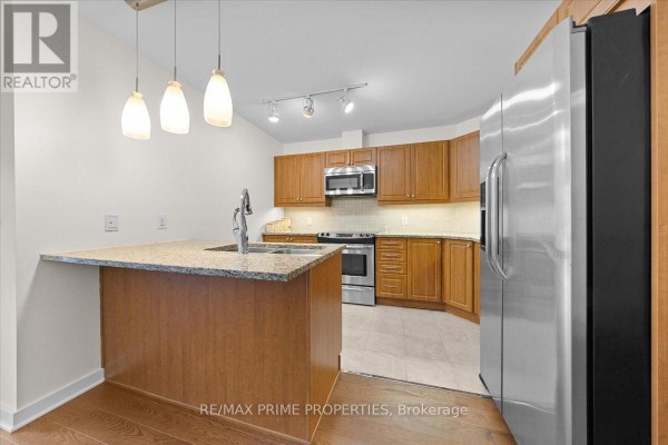 Living and dining area with glass table, chairs, and view of kitchen with wooden cabinets and granite counters. - 506 - 310 Centrum Boulevard, Ottawa