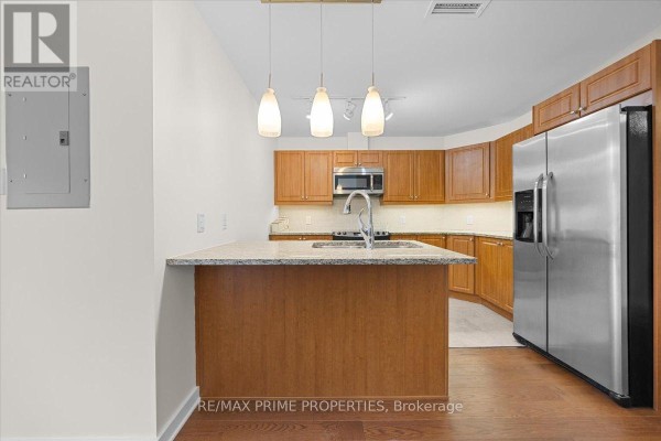 View of the kitchen area with wooden cabinets, stainless steel appliances, granite countertops, and island with sink. - 506 - 310 Centrum Boulevard, Ottawa