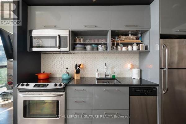 Open-concept living space with a white sofa, kitchen with grey cabinets and stainless steel appliances. - 506 - 51 Trolley Crescent, Toronto
