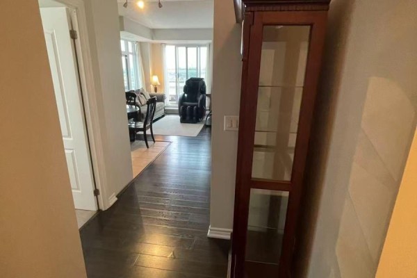 View from hallway into an open-concept living and dining area with large windows and dark hardwood floors. - 506 - 8323 Kennedy Road, Markham