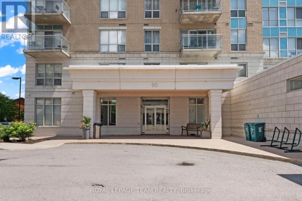 Close-up of the main entrance of a modern apartment building with beige stone and glass doors. - 506 - 90 Landry Street, Ottawa