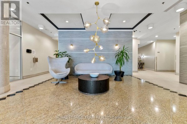 Apartment building lobby with a grey sofa, egg chair, coffee table, and patterned floor. - 506 - 90 Landry Street, Ottawa