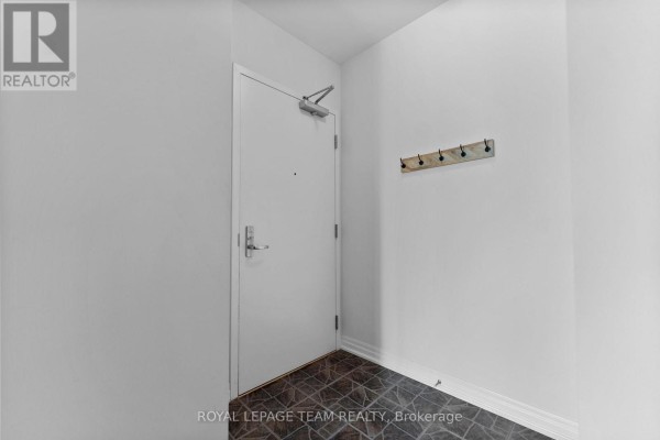 Interior hallway with a white door, coat hooks on a wooden rack, and dark tiled floor. - 506 - 90 Landry Street, Ottawa