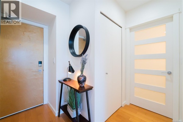 Apartment entryway with a wooden door, console table, round mirror, and a frosted glass door. - 506 38 Front St, Nanaimo