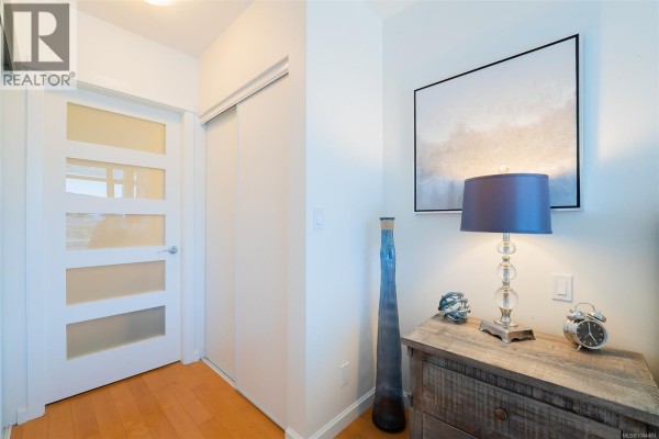 Apartment hallway with a frosted glass door, sliding closet, and decorative items on a dresser. - 506 38 Front St, Nanaimo