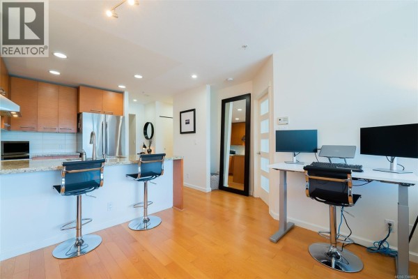 Kitchen island with bar stools, a home office setup with computers, and wooden floors. - 506 38 Front St, Nanaimo